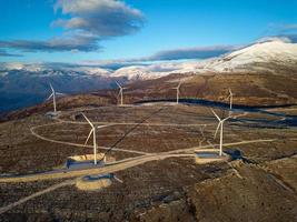 molinos de viento en las colinas durante la puesta de sol. energía renovable, energía verde. montañas en el fondo con nieve. energía eólica y respetuoso con el medio ambiente. Futuro sostenible. acabar con los combustibles fósiles. foto