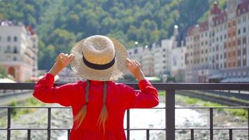 Little girl at hat on the embankment of a mountain river in a European city. video