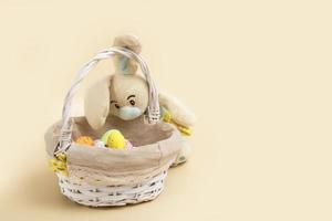 bunny peeks into an easter basket with eggs on a beige background with copy space photo
