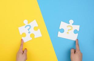 female hand holds a fragment of a white large puzzle on a yellow blue background, concept of finding an idea photo