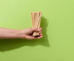 female hand holds disposable wooden sticks for stirring hot drinks on a green background. Coffee and tea spoon photo