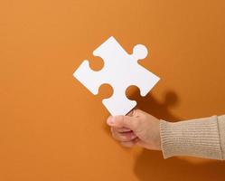 female hand holds a fragment of a white large puzzle on a brown background, the concept of finding an idea, solving a problem photo