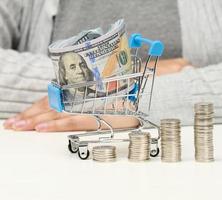 woman sits at a table, stacks of white coins and a miniature cart with US dollars. Concept of savings, sale, tax photo