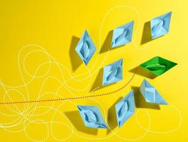 a group of blue paper boats and one green with paths on a yellow background. The concept of a strong leader with extraordinary thinking photo