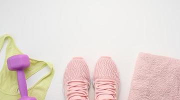 a pair of pink sneakers, a terry towel and a plastic dumbbell on a white background, top view photo