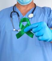 doctor in blue uniform and latex gloves holds a green ribbon photo