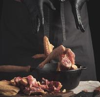 chef in black uniform and latex gloves chopping throws sliced chicken into a black cast-iron frying pan with a wooden handle photo