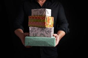 adult man in a black shirt holds in his hands a stack of paper-wrapped gifts on a black background photo