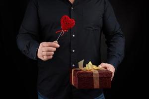 an adult man in a black shirt holds in his hand a red cardboard box tied with a golden bow photo