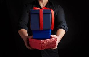 adult man in a black shirt holds in his hands a stack of paper-wrapped gifts on a black background photo