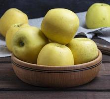 ripe whole yellow apples in a wooden bowl photo