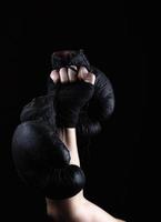 raised up man's hand holds a pair of old black leather boxing gloves photo