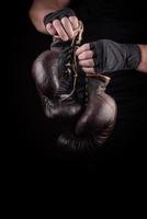sportsman in black uniform holds old vintage leather boxing gloves photo