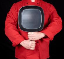 cook in red uniform holding an empty square black frying pan photo