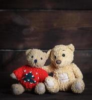 two brown soft teddy bears are sitting on a wooden surface photo