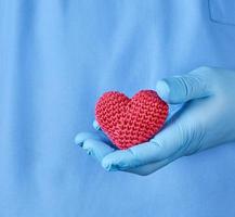 doctor with blue latex gloves holding a red heart photo