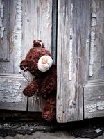 brown teddy bear peeks out from behind an old door with cracked paint photo