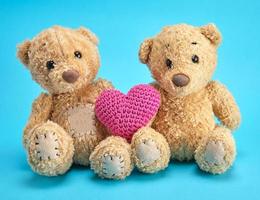 two brown teddy bears hold a red knitted heart on a blue background photo