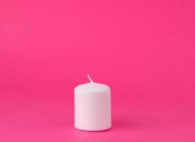 new white wax candle on a pink background photo