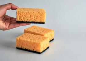 hand is holding a yellow kitchen sponge for washing dishes photo