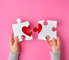 Female hands hold big white puzzles with a piece of red heart photo