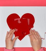 Female hands hold big white puzzles with a piece of red heart photo