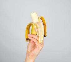 peeled fresh banana in a female hand on a white background photo