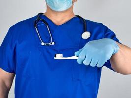 médico con guantes de látex estériles y uniforme azul sosteniendo un cepillo de dientes foto