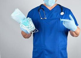 médico con uniforme y guantes de látex azules mantiene máscaras estériles foto