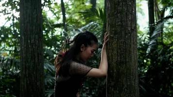 müde asiatische Frau, die sich auf dem großen Baum im Dschungel ausruht video