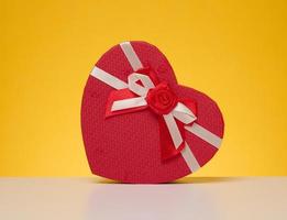 Red cardboard gift box in the shape of a heart on a yellow background photo