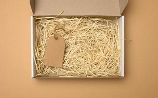 empty rectangular open corrugated paper box with sawdust inside. Packaging, containers for transportation on a brown background photo