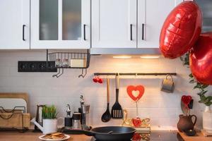 el interior de la cocina de la casa está decorado con corazones rojos para el día de san valentín. decoración en la mesa, estufa, utensilios, ambiente festivo en un nido familiar foto