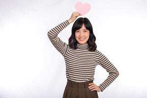 Beautiful young asian woman holding a paper heart while standing against white background. Beautiful young asian woman with paper heart. photo