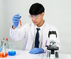 estudiante científico asiático en un laboratorio de mezcla de reactivos en un laboratorio de investigación científica con tubos de ensayo de varios tamaños y microscopios. sobre la mesa en el fondo blanco de laboratorio de química de laboratorio. foto