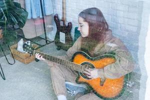 Young woman playing guitar at home, view through the glass window photo