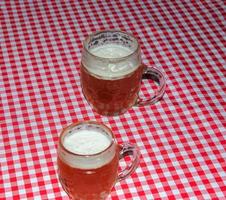una jarra de cerveza sobre una mesa cubierta con un mantel a cuadros rojos. foto