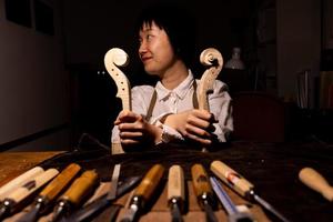 young chinese woman violin maker showing the neck of the violins under construction photo