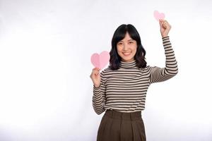 hermosa joven asiática sosteniendo un corazón de papel mientras se enfrenta a un fondo blanco. hermosa joven asiática con corazón de papel. foto
