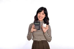 retrato de joven asiático mujer casual uniforme participación blanco cerdito banco y calculadora aislado en blanco fondo, financiero y banco ahorro dinero concepto foto