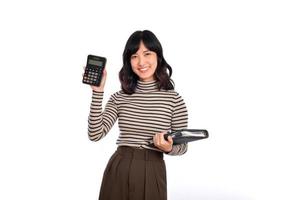 Portrait of young Asian woman casual uniform holding white piggy bank and notebook isolated on white background. Financial and bank saving money concept photo