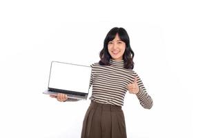 hermosa joven asiático mujer en suéter paño participación ordenador portátil ordenador personal computadora y mirando a cámara con sonrisa cara y pulgar arriba, aislado en blanco antecedentes foto