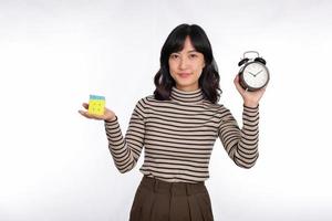 Asian woman holding alarm clock and rubik cube standing on white background. solving cubic problems, problem solution and making strategic moves concept photo