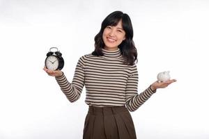 contento asiático mujer con suéter camisa participación alarma reloj y cerdito banco aislado en blanco antecedentes foto