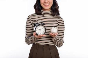 contento asiático mujer con suéter camisa participación alarma reloj y cerdito banco aislado en blanco antecedentes foto