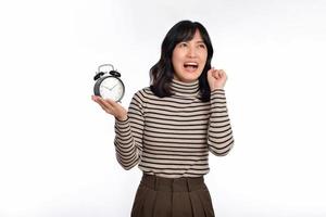 Portrait of excited young Asian woman with sweater shirt holding alarm clock isolated on white background photo