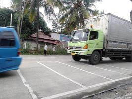 Bogor, Indonesia, 2023 - Blue car and truck on road with coconut tree nature background represent indonesian view photo