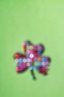 St. Patrick's Day minimalistic concept. Blurred clover leaf on green background with colorful bokeh photo