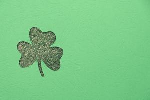 St. Patrick's day minimalistic concept. Clover leaf shape from textured paper and glitter background with copy space photo