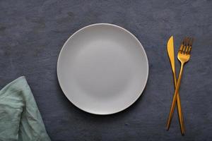 Grey empty plate, cutlery and napkin on dark stone table. Top view, Table setting. background for menu, layout, place for text, recipe background, food flat lay background photo
